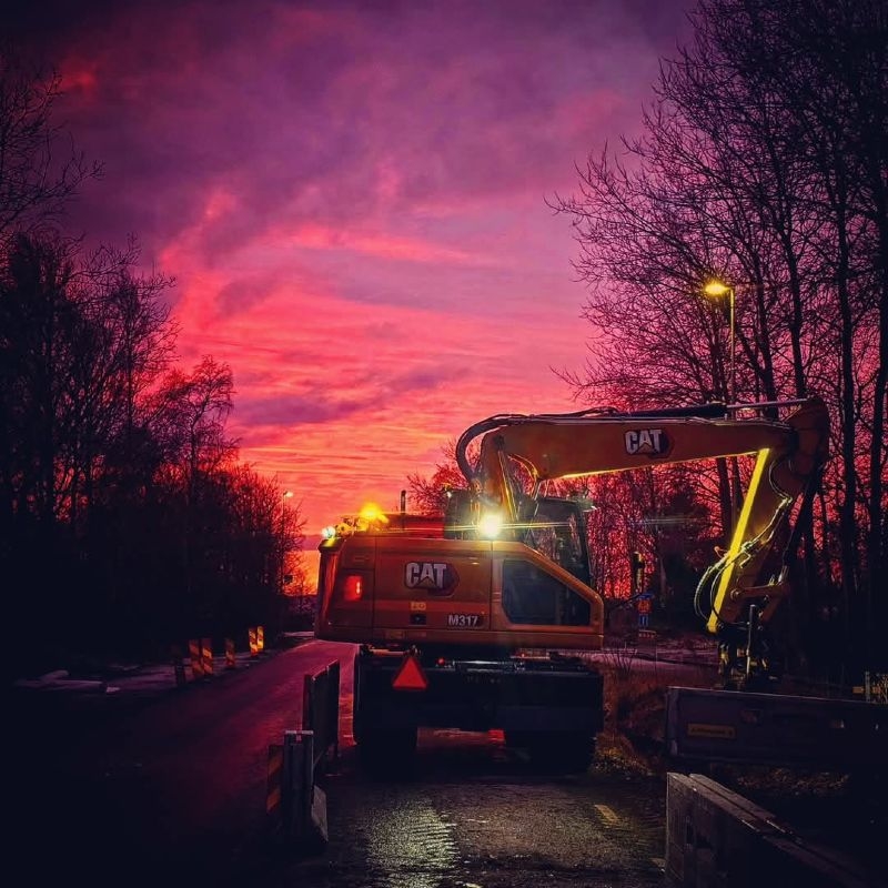 Grävmaskin arbetar i solnedgången.